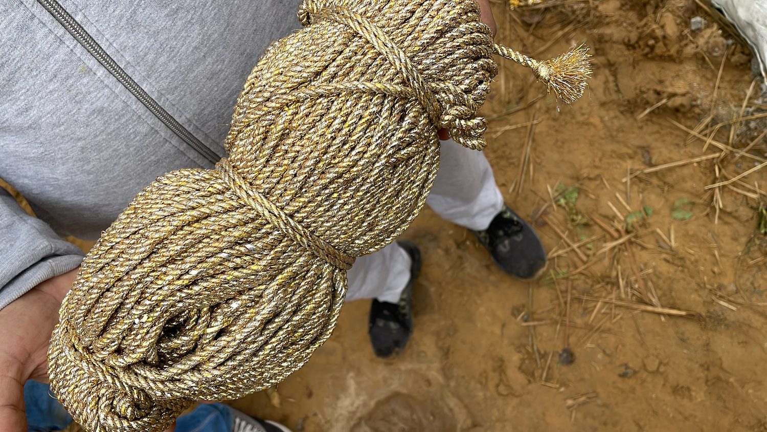 A thick coil of hand-twisted rope lying on bare earth beside somebody's feet