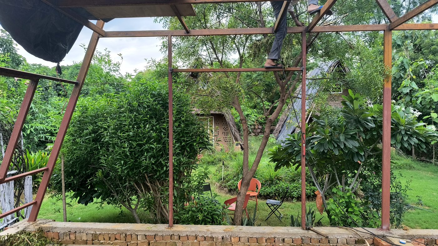 A steel frame standing open to the sky in dense green planting, chairs beneath it