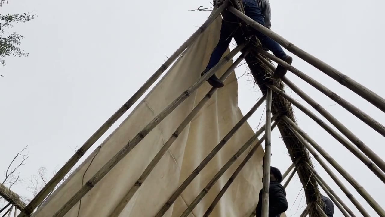 Bamboo A-frame going up, a thatch panel being woven by hand, and a crane lifting a thatch roof into place