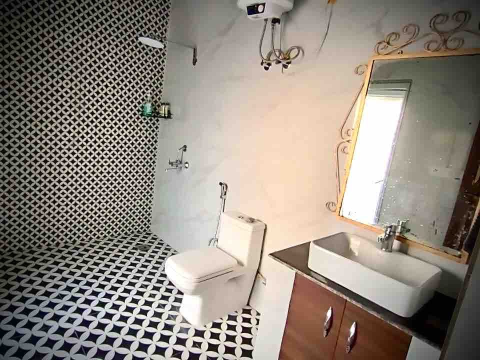 A tiled bathroom with a washbasin on a wooden cabinet, mirror, WC and a patterned floor