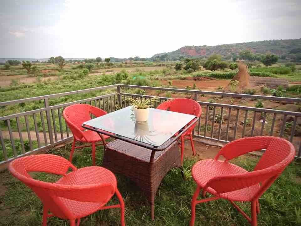 Red chairs round a table on a railed terrace looking out over scrub to the Aravalli ridge