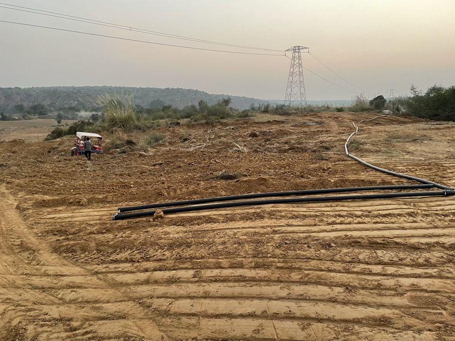 A black pipe laid along ploughed contours, a pylon on the horizon