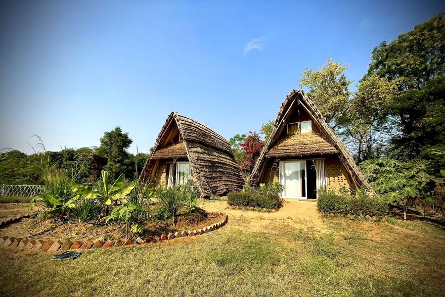 Two thatched A-frame huts in a green garden under a blue sky